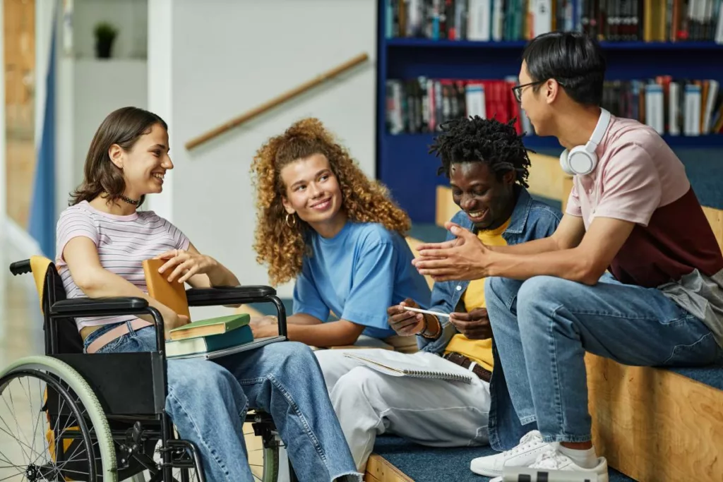 Groupe d’étudiants souriants, dont une jeune femme en fauteuil roulant, illustrant l’inclusion scolaire et la reconnaissance handicap dans l’enseignement en Belgique.